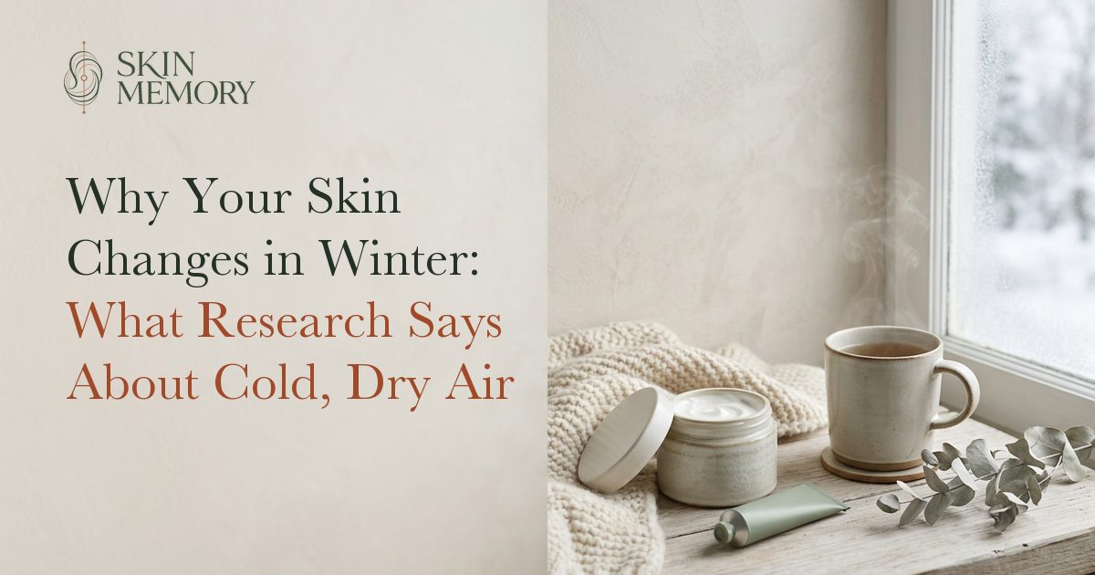 An open jar of rich moisturiser, a tube and a cup of tea on a knitted blanket by a frosted window, illustrating how skin changes in winter